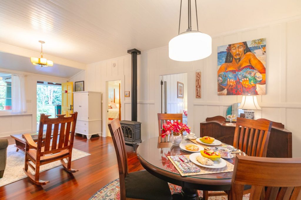 dining room with breakfast fare on the table, hawaiian print on the wall and part of the living room with fireplace.