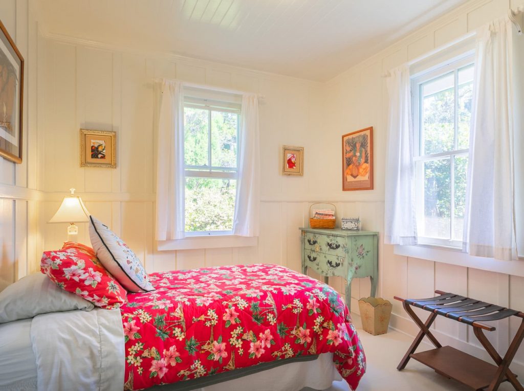 second bedroom with single bed, red bedspread and two windows bringing sunshine into the room.