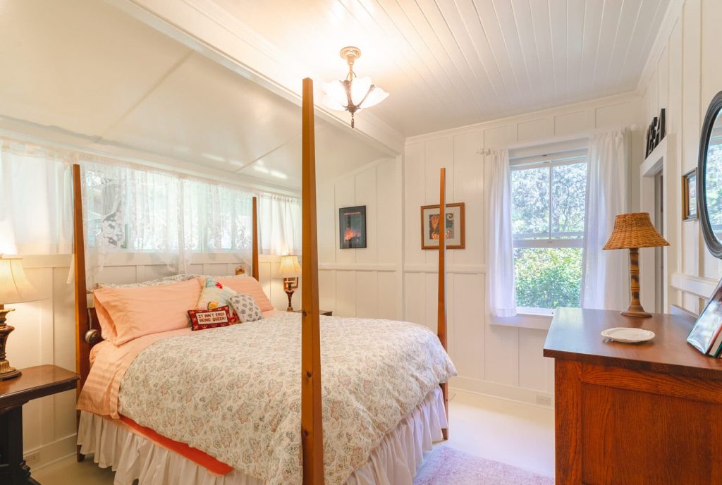light filled bedroom with four poster bed, dresser and side tables.